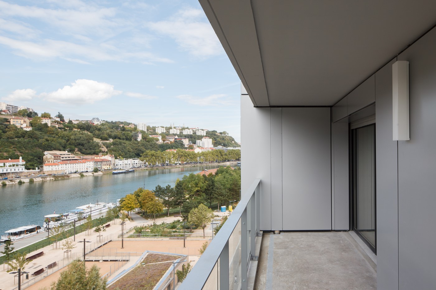 View from a modern balcony over the quays of the Saône in Lyon, with colourful riverside buildings and a wooded hill in the background.