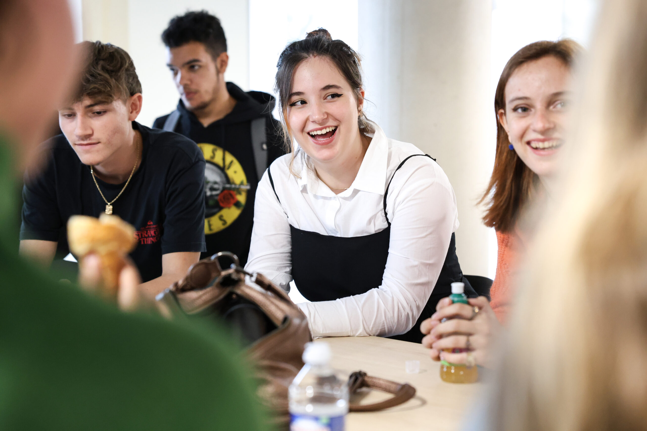 Groupe d’étudiants assis autour d’une table en train de discuter et de rire dans une ambiance détendue et chaleureuse.