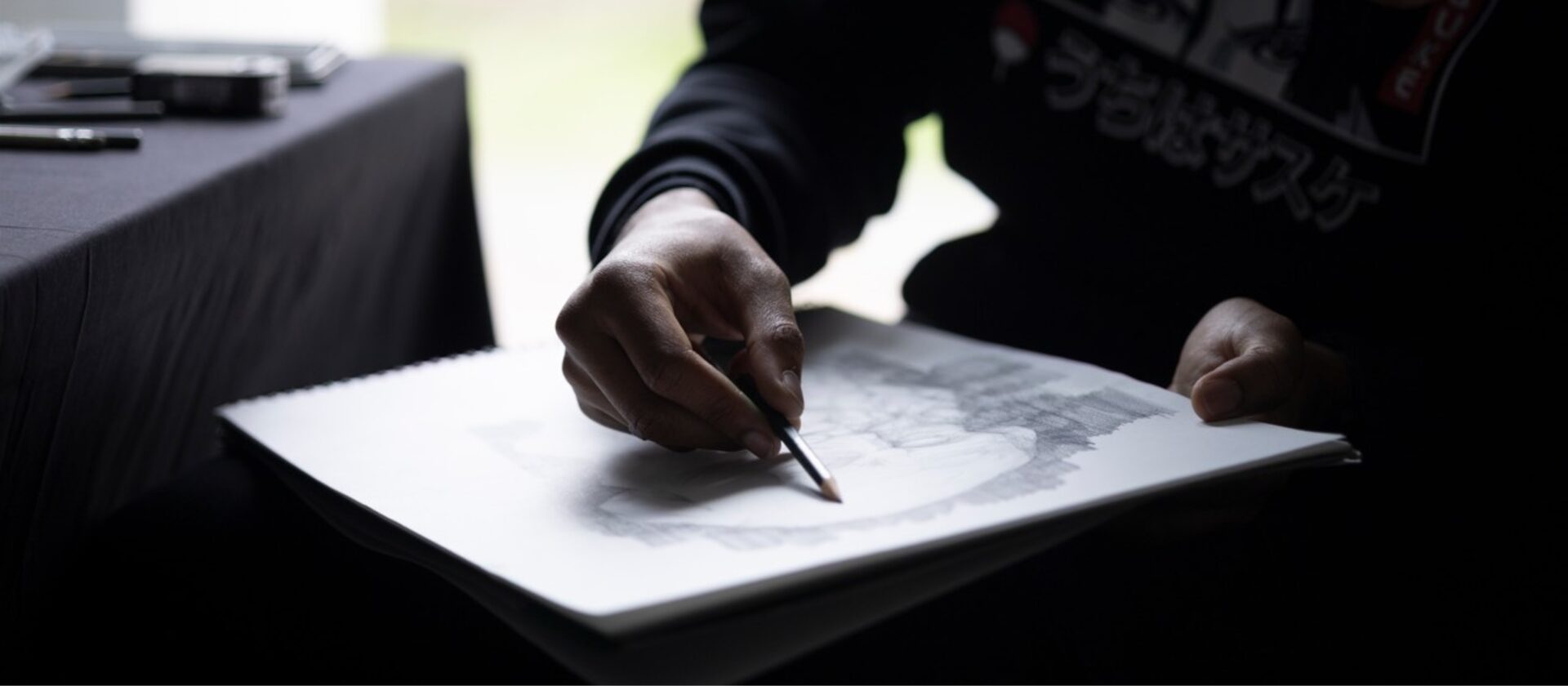 Gros plan sur une main dessinant au crayon sur un carnet.