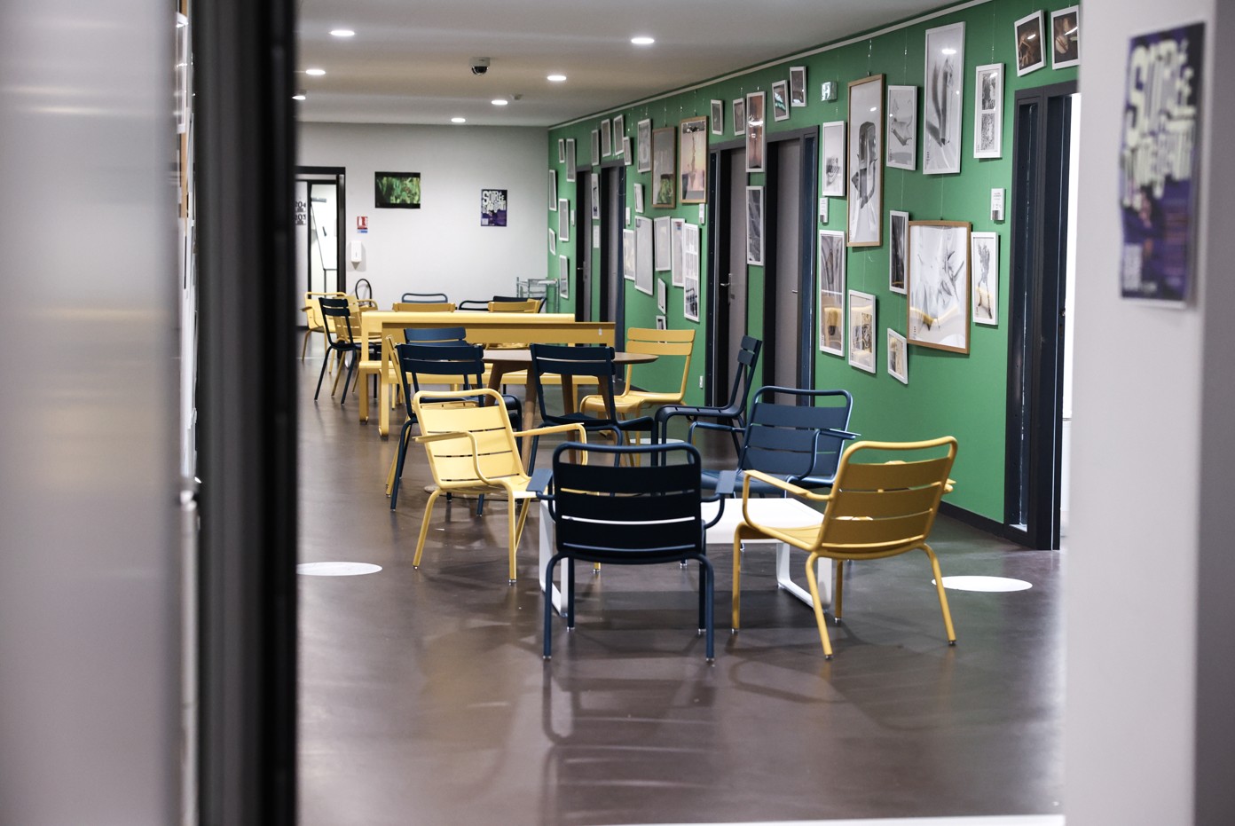 A room for relaxing or working, with colourful chairs and tables, and artwork hanging on the green wall at the back.