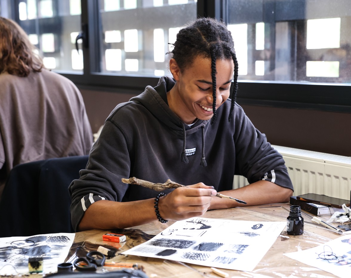 Étudiant souriant en cours de dessin, travaillant à l’encre sur papier.