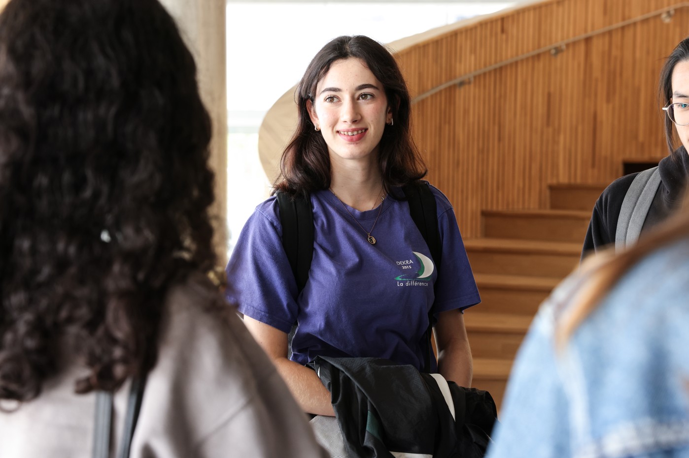 Étudiante souriante en discussion avec d’autres étudiants dans un hall.