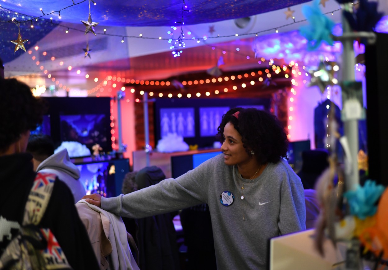 ESMA student talking to visitors in a room decorated with string lights and illustrations.