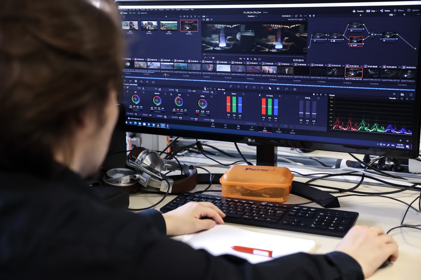 A student works on video editing and colour-grading software, displayed on a large screen with colour curves and a timeline.
