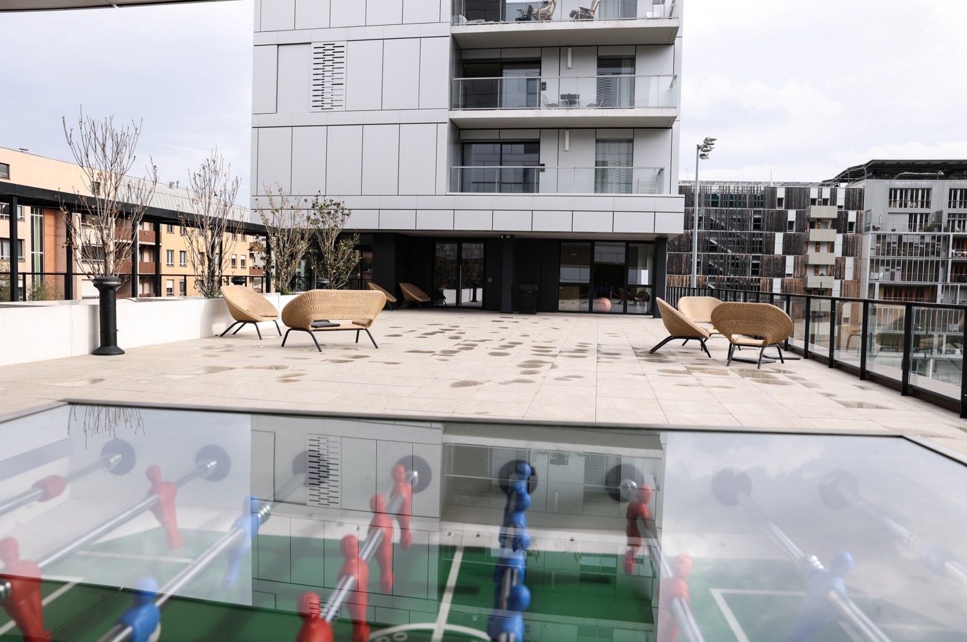 Large outdoor terrace with rattan armchairs, overlooking modern buildings, with table football in the foreground.